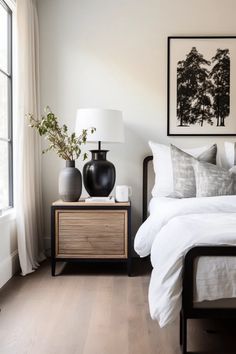 a bedroom with white bedding and black vases on the nightstand next to it