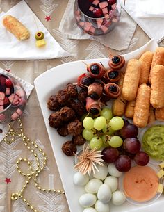 an assortment of food is displayed on a white platter with grapes, meatballs and crackers