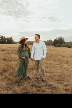 a pregnant couple holding hands and standing in a field