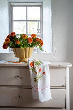 an old dresser with flowers on it and a towel hanging from the handle, in front of a window