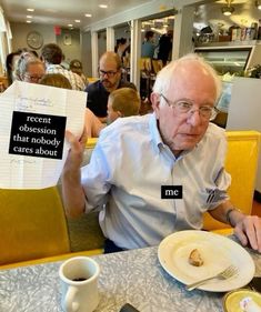 an older man sitting at a table holding up two signs with words written on them