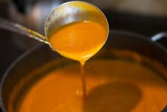 a spoon full of orange liquid being poured into a pot