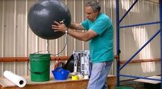 a man is holding an exercise ball in his right hand while standing on a shelf