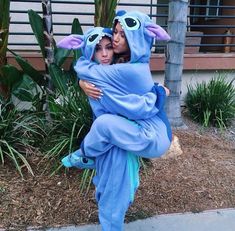 two people dressed in costumes hugging each other on the side of a street with palm trees and bushes behind them