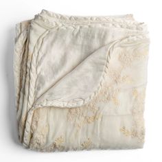 a white blanket with gold embroidered flowers on it and a ruffled edge is folded up