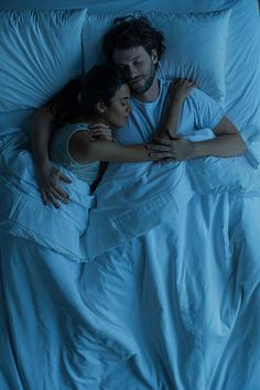 a man and woman cuddling in bed under the covers with blue light shining on them