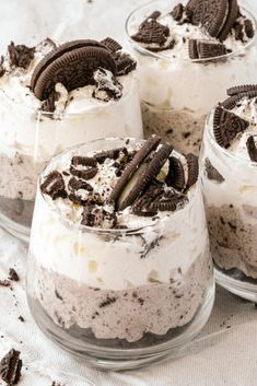 three desserts with oreo cookies and cream in glass dishes on a white cloth