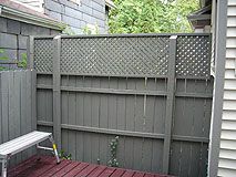 a wooden deck with a white bench next to a gray fenced in backyard area