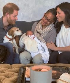 three people sitting on a couch with a baby and two dogs