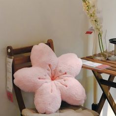 a pink flower shaped pillow sitting on top of a chair next to a wooden table