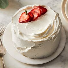 a white cake topped with strawberries on top of a plate next to a fork