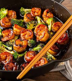 shrimp and broccoli stir fry with chopsticks in a black skillet