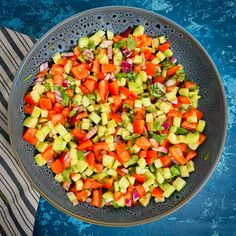 a large bowl filled with chopped vegetables on top of a table next to a towel