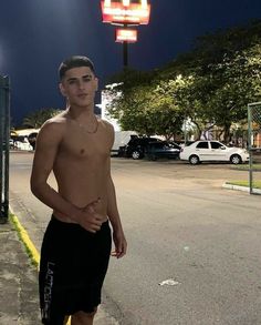 a shirtless young man standing on the side of a road at night with his hands in his pockets