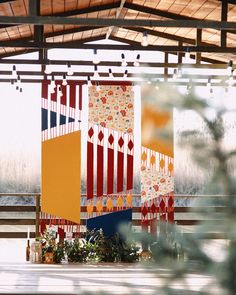 an outdoor area with several colorful pieces of art hanging from the ceiling and plants in front of it