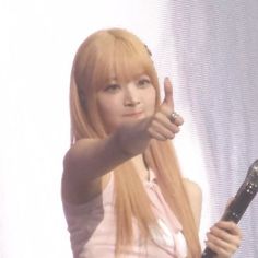 a woman with long red hair is holding a microphone and giving the peace sign while standing in front of a screen