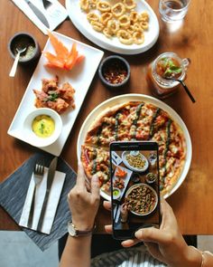 a woman taking a photo of food on her phone at a table with other plates and bowls