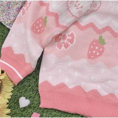 two sweaters laying on the grass next to flowers and sunflowers with hearts