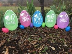 easter eggs with names painted on them sitting in the ground next to a tree and grass