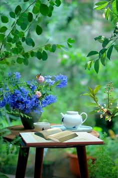 a table with flowers and an open book on it in front of a forest background