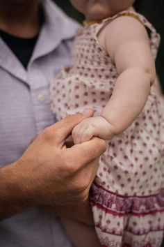 a man holding a small baby in his arms while he holds the hand of it's mother