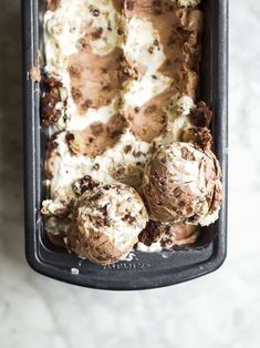 an ice cream sundae in a black container on a marble counter top with chocolate chunks and marshmallows