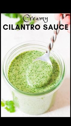 a hand holding a spoon over a jar filled with creamy cilantro sauce