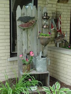 an outdoor garden with pots and watering cans on the side of a house, surrounded by flowers