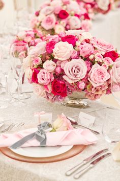 the table is set with silverware and pink flowers in vases on top of it