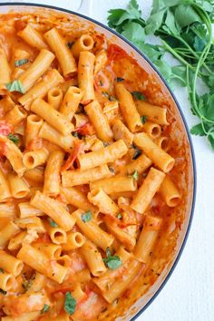 a bowl filled with pasta and parsley on top of a white table next to a green leafy garnish