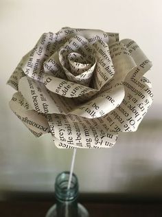 a paper rose sitting on top of a glass vase filled with water and newspaper strips