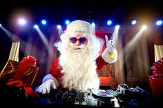 a dj dressed as santa clause in front of christmas presents