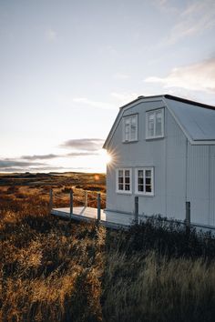 a white house sitting on top of a grass covered field next to a wooden fence