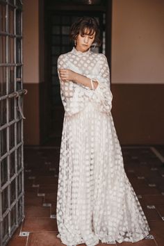 a woman wearing a white dress standing in front of an open door with her arms crossed