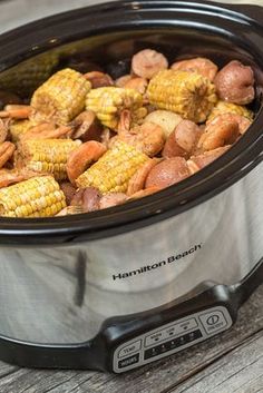 a crock pot filled with cooked corn and potatoes on top of a wooden table