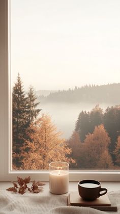 a candle sitting on top of a wooden table next to a window sill filled with autumn leaves