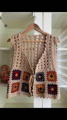 a crocheted vest hanging on a wooden hanger in front of a shelf