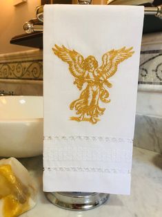 a white towel with gold embroidered angel on it sitting next to a sink in a bathroom