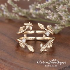 two gold rings sitting on top of a wooden table next to some flowers and leaves