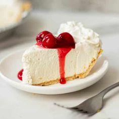 a white plate topped with a slice of cheesecake covered in whipped cream and cherries