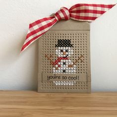 a small bag with a cross - stitch snowman on it and a red ribbon