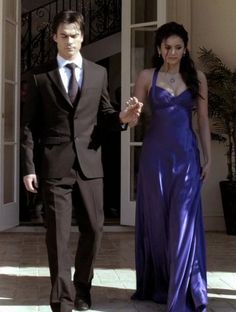 a man in a suit and tie walking next to a woman in a purple dress