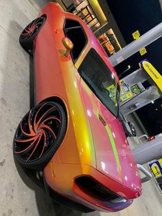 an orange and pink car parked in front of a gas station with its hood up