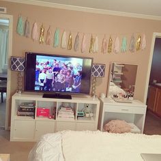 a flat screen tv sitting on top of a white dresser next to a wall with tassels hanging from it