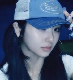 a woman with long black hair wearing a blue and white baseball cap holding her hand up to her ear