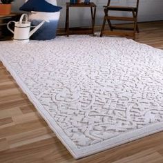 a large white rug on top of a hard wood floor next to a chair and table