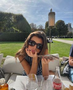 a woman sitting at a table with drinks and food in front of her, wearing sunglasses