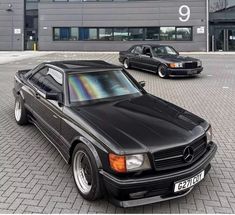 two black mercedess parked in front of a building with windows on the side of it