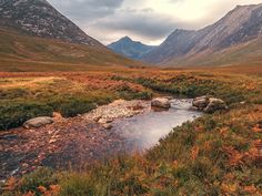 a small stream running through a lush green valley with mountains in the backgroud