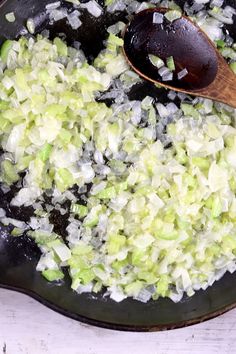 a wooden spoon is in a skillet filled with chopped up cabbage and onions on a white table